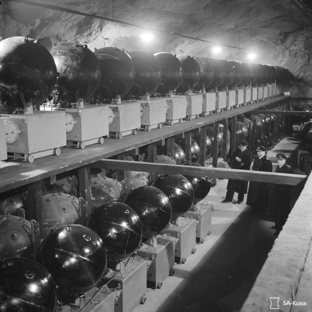 Miinatunneli, jossa usieta miinoja rivissä. Henkilöitä katsomassa miinoja.