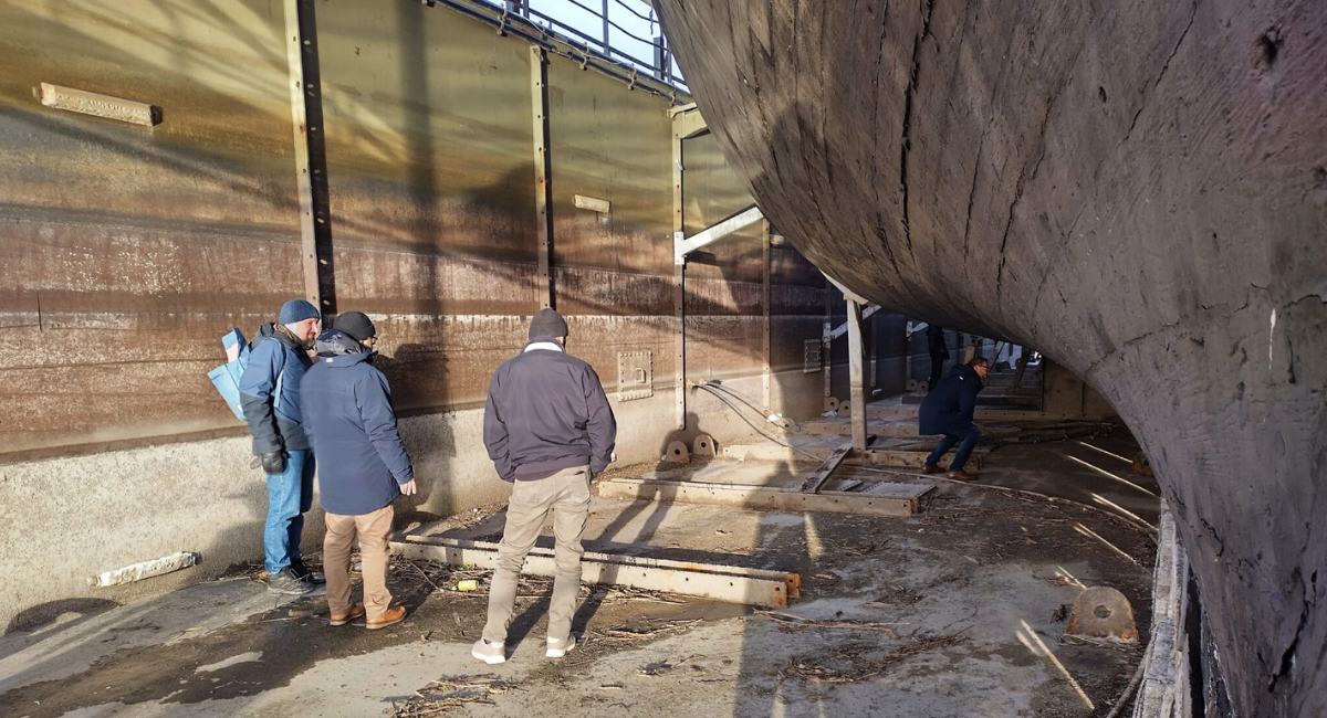 Neljä henkilöä museolaiva Sigynin telakan pohjalla tutkimassa laivan pohjaa.